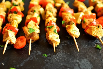 Traditional greek dish souvlaki. Kebabs on wooden skewers. Shish kebabs with tomatoes, mushrooms, pepper and lemon, top view, black concrete background. Place for text.