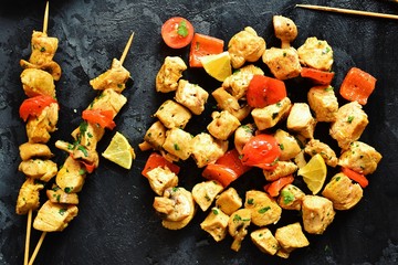 Traditional greek dish souvlaki. Kebabs on wooden skewers. Shish kebabs with tomatoes, mushrooms, pepper and lemon, top view, black concrete background. Place for text.
