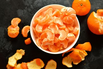 Juicy and ripe tangerines on a dark background. Tangerine slices in a white bowl, top view. Peeled tangerine. Tasty fruits. Horizontal view 