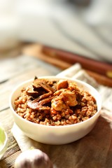 Buckwheat porridge in a white bowl. Buckwheat porridge with mushrooms and chicken breast. Wooden background and linen napkin. Vertical view 