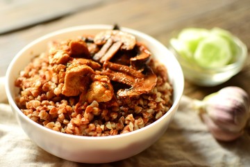 Buckwheat porridge in a white bowl. Buckwheat porridge with mushrooms and chicken breast. Wooden background and linen napkin.