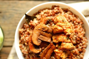 Buckwheat porridge in a white bowl. Buckwheat porridge with mushrooms and chicken breast. Wooden background and linen napkin. Top view 