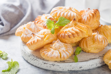 Profiterole or gougeres  or eclair with custard cream filling served for breakfast on a white plate with tea on a concrete table, view from above, close-up