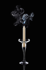 extinct white candle in glass candlestick with smoke on black background