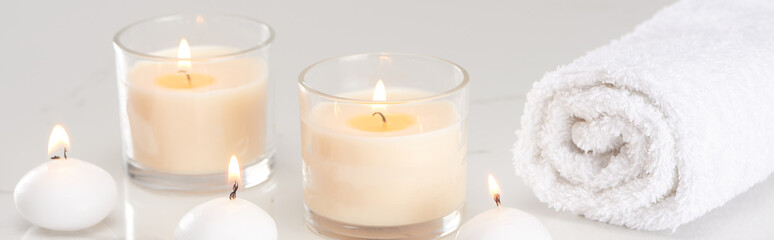 burning white candles in glass and rolled towel on marble white surface, panoramic shot