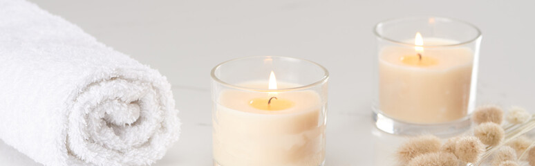 fluffy bunny tail grass near burning white candles in glass and rolled towel on marble white surface, panoramic shot