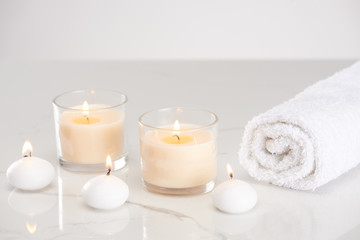 Fototapeta na wymiar burning white candles in glass and rolled towel on marble white surface
