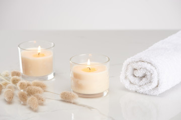 Fototapeta na wymiar fluffy bunny tail grass near burning white candles in glass and rolled towel on marble white surface
