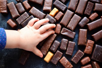 Assortment of chocolates. Top view place for text. Dark chocolate. Hands in the frame. Baby and candy. Girl takes chocolate candy with hands.