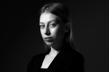 Blonde with long hair in a black suit on black background, black and white. Business woman