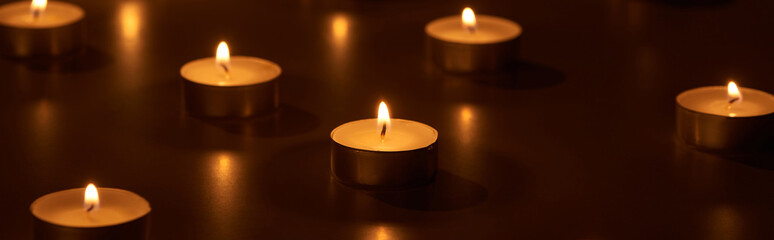 selective focus of burning white candles glowing in dark, panoramic shot