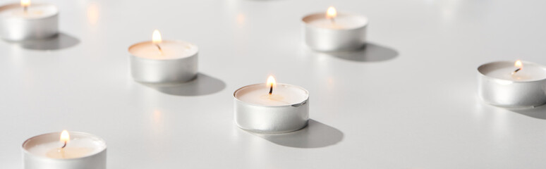 Fototapeta na wymiar selective focus of burning candles glowing on white surface, panoramic shot