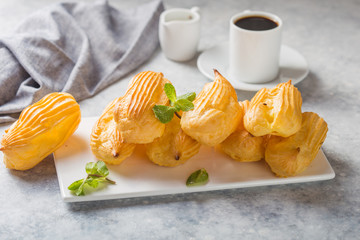 Profiterole or gougeres or eclair with custard cream filling served for breakfast on a white plate with tea on a concrete table, view from above, close-up