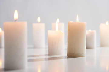 Fototapeta na wymiar selective focus of burning white candles on white surface glowing isolated on grey