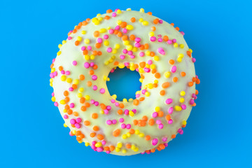 Glazed yellow donut with a hole on blue background. Unhealthy calorie food concept. Fun mood.