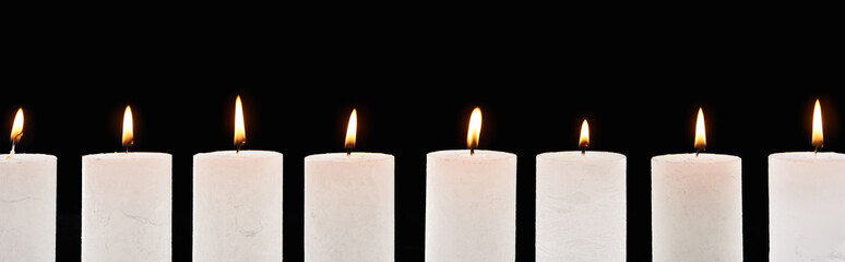 burning white candles glowing in line isolated on black, panoramic shot