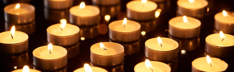 selective focus of burning candles glowing in darkness, panoramic shot