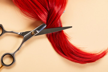 Top view of scissors and curl of red hair on beige background