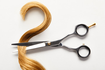 Top view of strand of brown hair with scissors on white background
