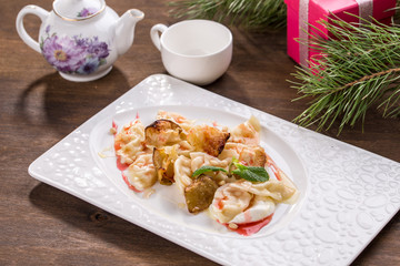 vareniki or dessert dumplings with apple and strawberry jam and cup of tea on wooden table