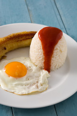 Fototapeta premium Arroz a la cubana Typical Cuban rice with fried banana and fried egg on a plate on wooden table. Close up
