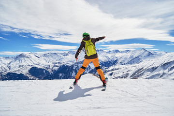 Fototapeta na wymiar Enthusiastic skier wearing colorful clothes and a green backpack, posing on a ski slope in Les Sybelles ski resort, with French Alps peaks in the background, on a day with perfect skiing weather.