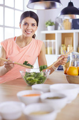 Smiling young woman mixing fresh salad in the kitchen.