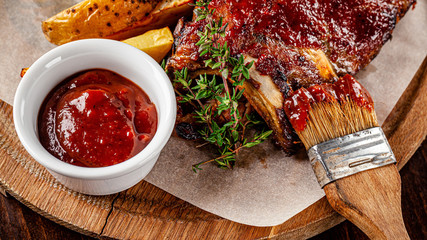 American cuisine. Fried pork and ribs in a marinade with homemade barbecue sauce, next to it lies a marinade brush. Serve on a wooden kitchen board. background image, copy space