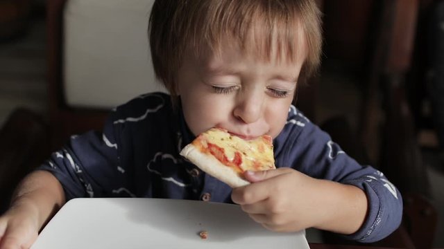 Close up of little cute boy eating pizza. Neutral colors for collor correction.