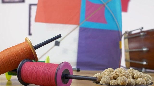 Beautifully decorated wooden table with Makar Sankranti items - festive scene. Racking focus of designer charkhi and til ladoos with a colorful kite and dholak for the celebration of Makar Sankrant...