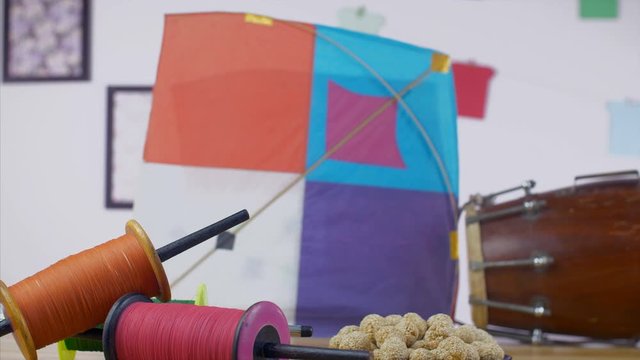 Pan shot of Makar Sankranti items during the celebration time in India - festive season. Beautifully decorated wooden table with dholak  til ladoos  designer charkhis  and colorful kites for Makar ...