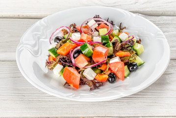 Greek salad in a white plate on a white wooden background