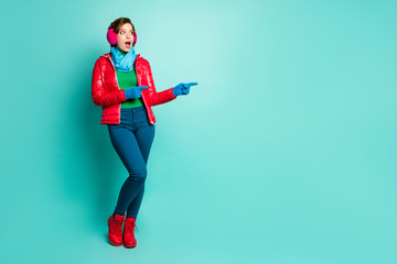 Full length photo of pretty lady directing fingers empty space offer sale low prices shopping wear red overcoat blue scarf pink ear muffs pants shoes isolated teal color background