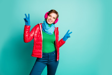 Photo of funny traveler lady enjoy sunny winter day rejoicing showing v-sign symbol skating wear casual red overcoat blue scarf pink ear covers trousers isolated teal color background