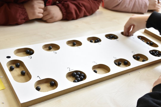 A table game of a beige color on a table: "mangala". and hands of people playing mangala