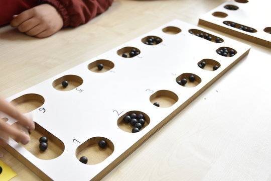 A table game of a beige color on a table: "mangala". and hands of people playing mangala