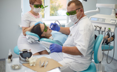 Fototapeta premium Doctor dentist treats teeth of a beautiful young girl patient. The girl on reception at the dentist. Doctor dentist treats tooth