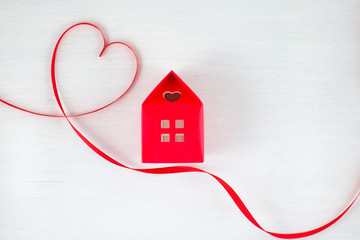 Red ribbon heart on a white wooden background, red house with a heart shape window in a romantic, valentine, family or wedding concept. Empty space for your text.