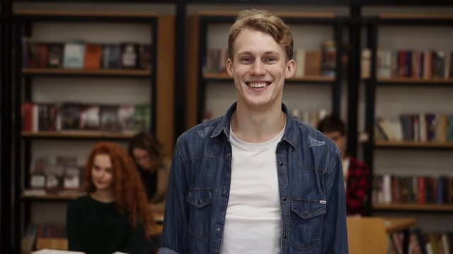 Close up portrait attractive young man laughing enjoying successful lifestyle achievement cheerful caucasian male in library bookshelf and classmates on background college education