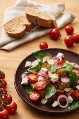 selective focus of delicious Italian vegetable salad panzanella served on plate on wooden table near fresh tomatoes and bread