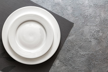 Empty white plate served on relief napkin and embossed gray concrete background. Top view mock up for menu