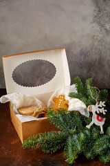 sweet Christmas gifts cookies, a jar of caramel lie in a gift box next to a spruce branch and a deer toy on a grunge background