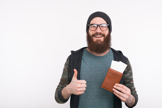 Photo of smiling man with beard showing thumbs up and holding passport and blank tickets