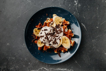 Viennese waffles on a plate, with a crumb of chocolate and slices of banana on a dark textured background.
