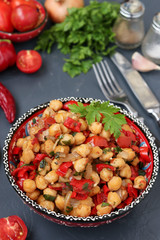 Garnish of chickpeas with pepper and tomatoes, a vegetarian dish rich in protein, located in a plate against a dark background, Vertical orientation