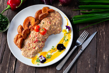 Stuffed chicken covered with paprika sauce, fried potatoes, edible garnish decoration, cutlery and vegetables