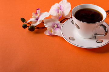 Obraz na płótnie Canvas cup of aromatic coffee and an orchid branch on an orange trendy background with space for text