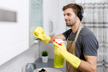 Young brunet lad cleaning the kitchen eagerly, listening to the music