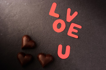 inscription love u and heart-shaped chocolates on a black background