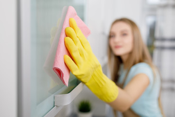 Close-up of young blonde woman in yellow gloves washing cupboard